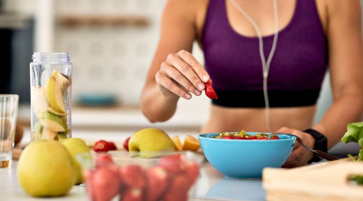 76 closeup athletic woman adding strawberries while making fruit salad kitchen min scaled 1