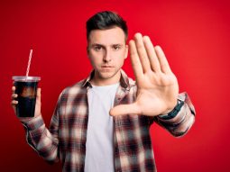 Young handsome caucasian man drinking a fresh soda refreshment over red background with open hand doing stop sign with serious and confident expression, defense gesture Depositphotos 363732264 L