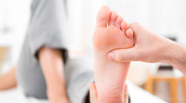 Young attractive physiotherapist doing reflexology on a patient feet Fascite Plantare