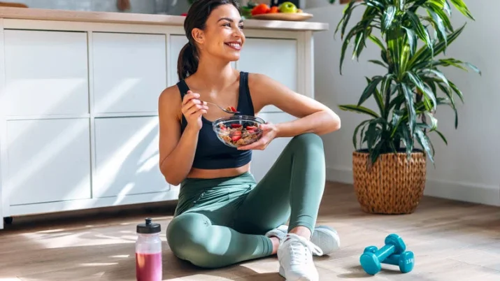 alimentazione antiage donna seduta per terra sorridente che mangia dopo aver fatto fitness