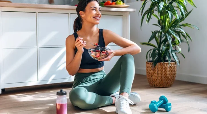 alimentazione-antiage-donna-seduta-per-terra-sorridente-che-mangia-dopo-aver-fatto-fitness alimentazione antiage donna seduta per terra sorridente che mangia dopo aver fatto fitness